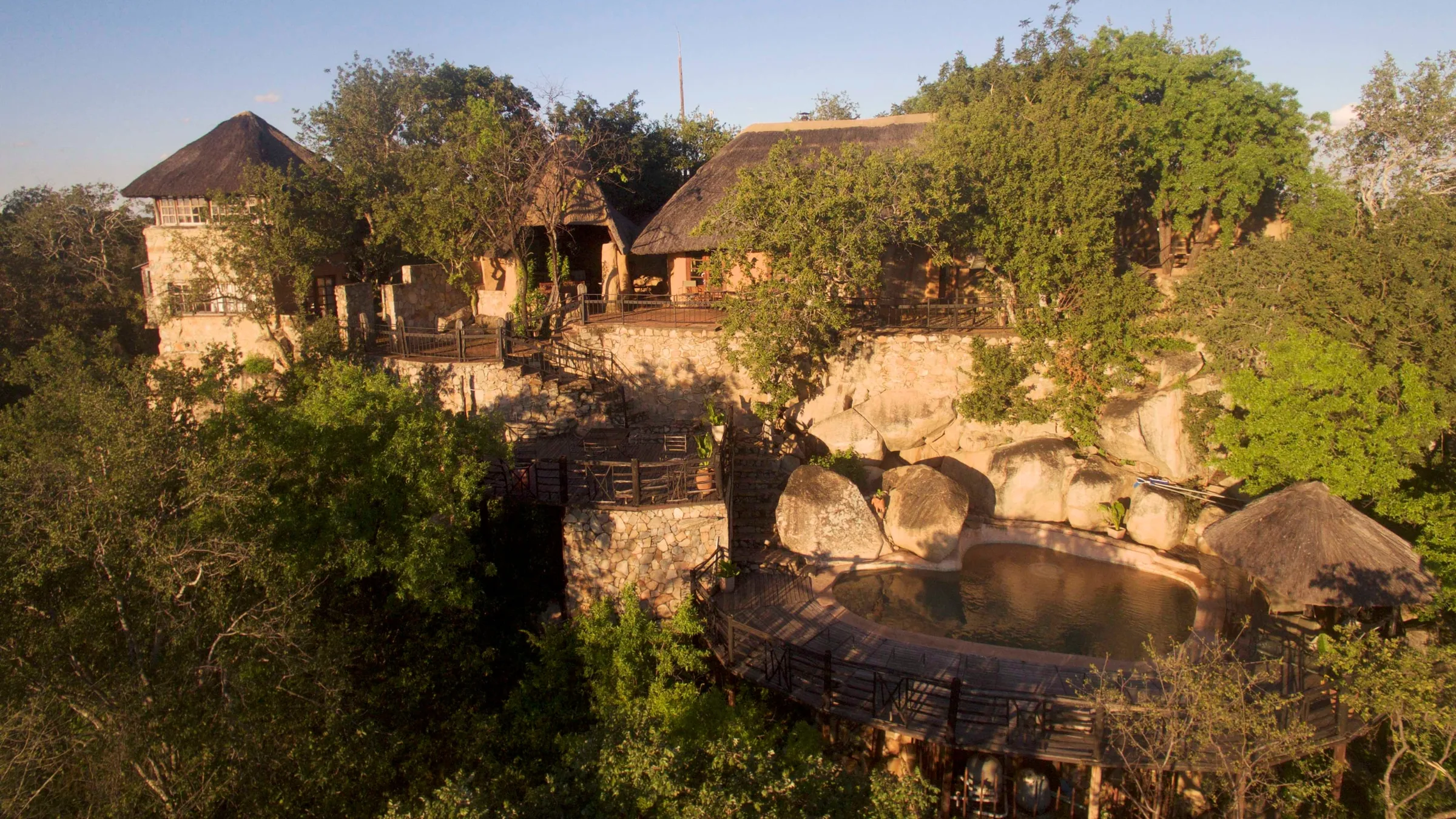 Khami Lodge from the air at golden hour, thatched roofs among the trees with the reserve beyond